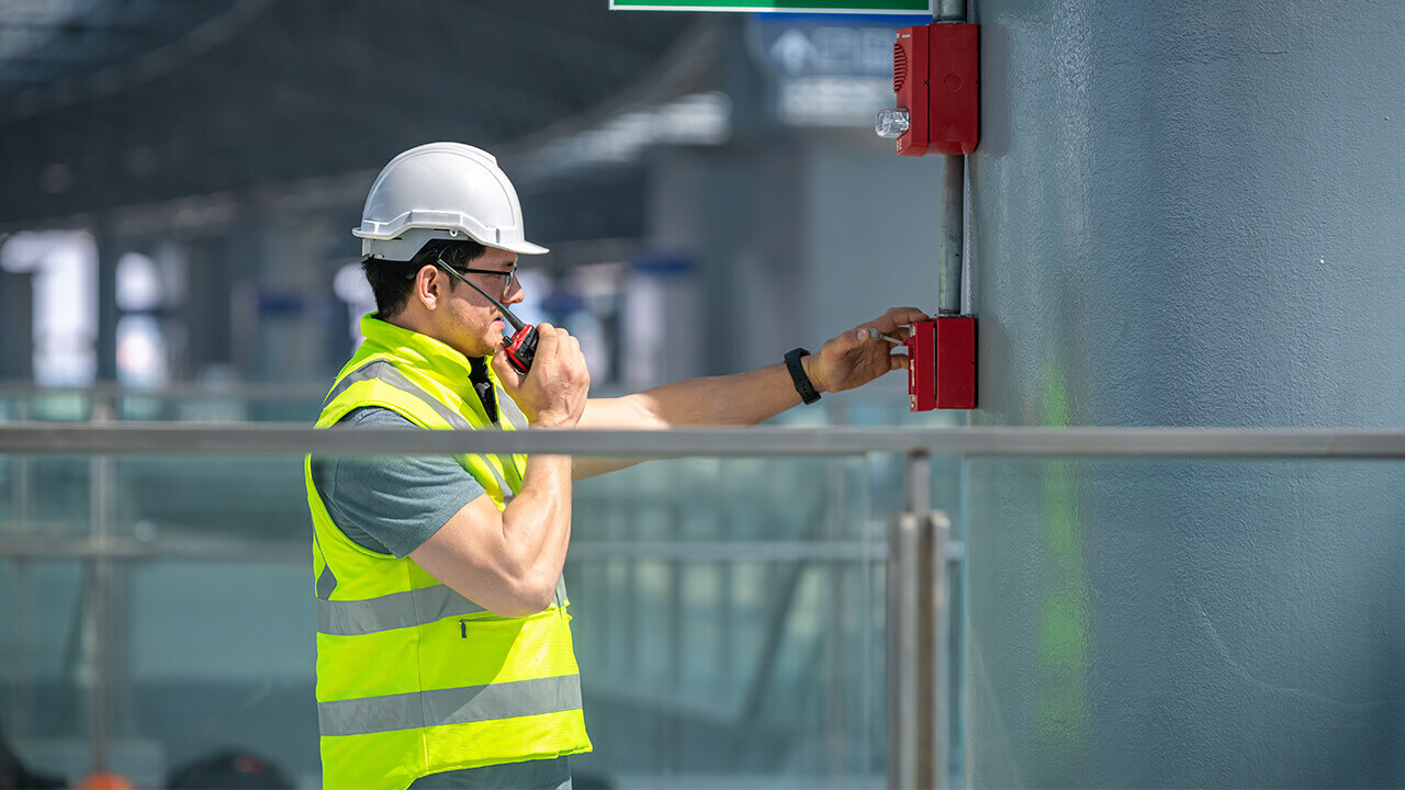 Engineer in safety uniform and helmet checks fire alarm emergency system in an industrial factory.