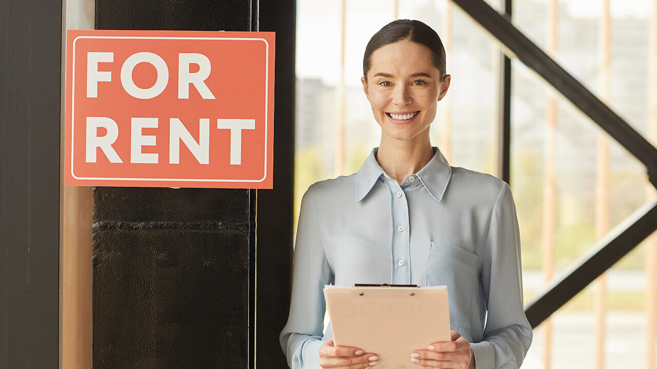 Waist-up portrait of a smiling female property manager posing next to a red