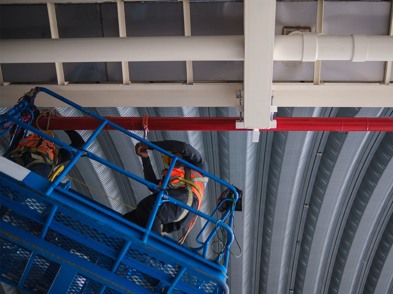 Fire sprinkler installation: Industrial plant. Red pipes by contractor using scissor lift for high reach.