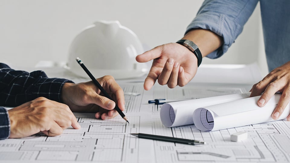 Two business man engineers drawing on blueprint and discussing a plan.